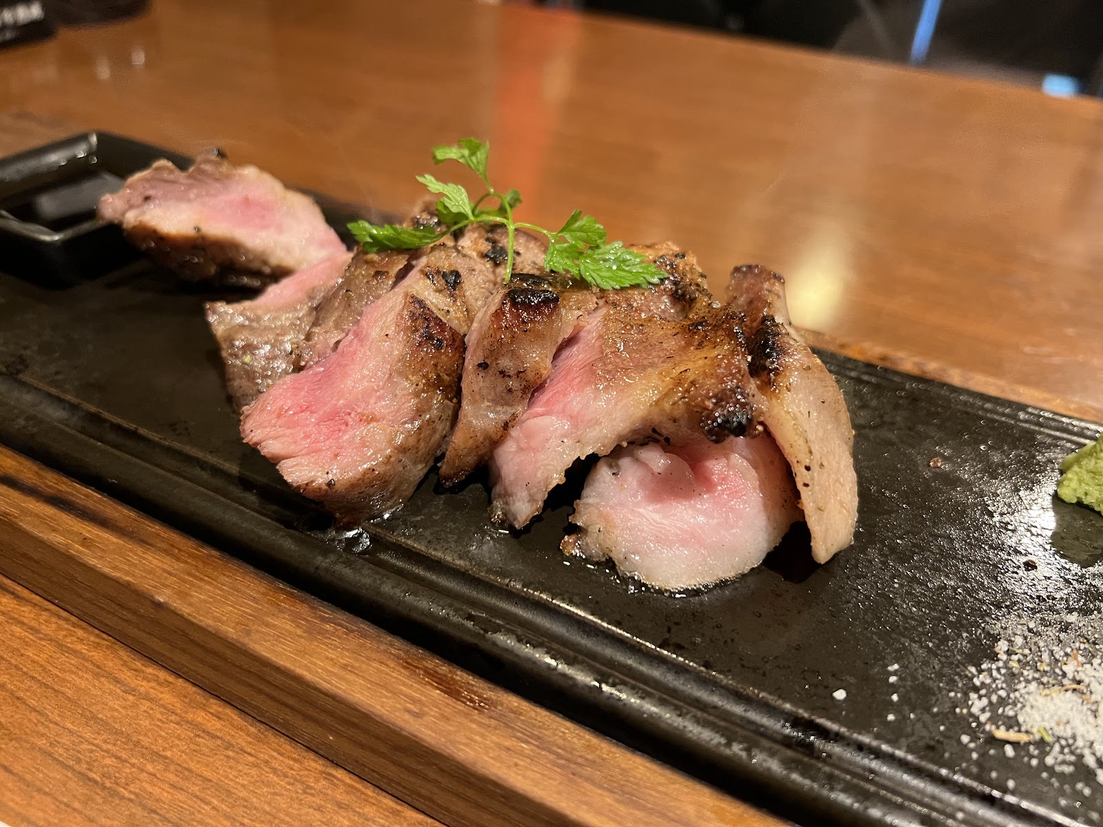 木のカウンターに置いた長い黒皿。スライスした豚のステーキとハーブ。