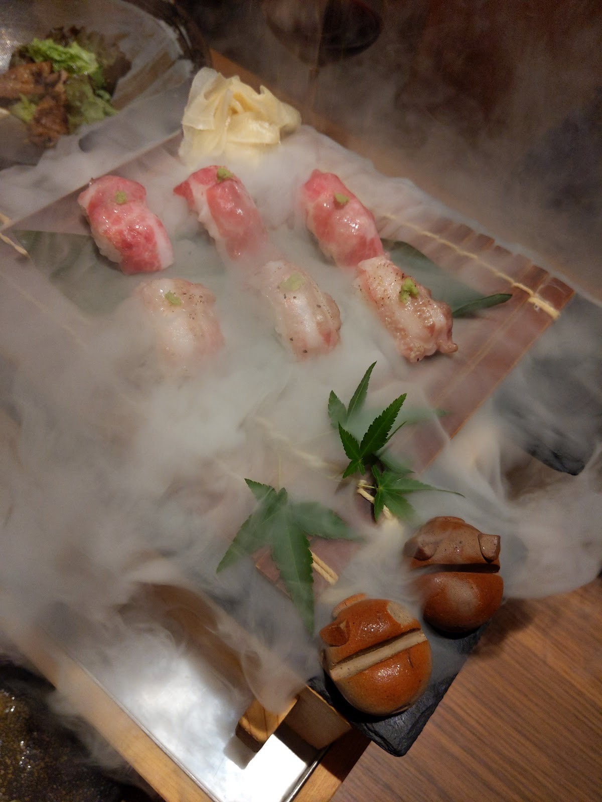 ドライアイスの白い霧の中に並んだ六貫の豚肉の握り。紅葉の葉、ガリ、二つの陶器の豚の置物。