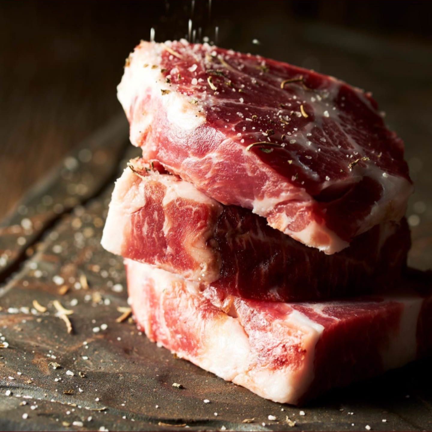 黒いスレートの上に重ねた三枚の厚切りの生の豚肉。塩の結晶が舞う。