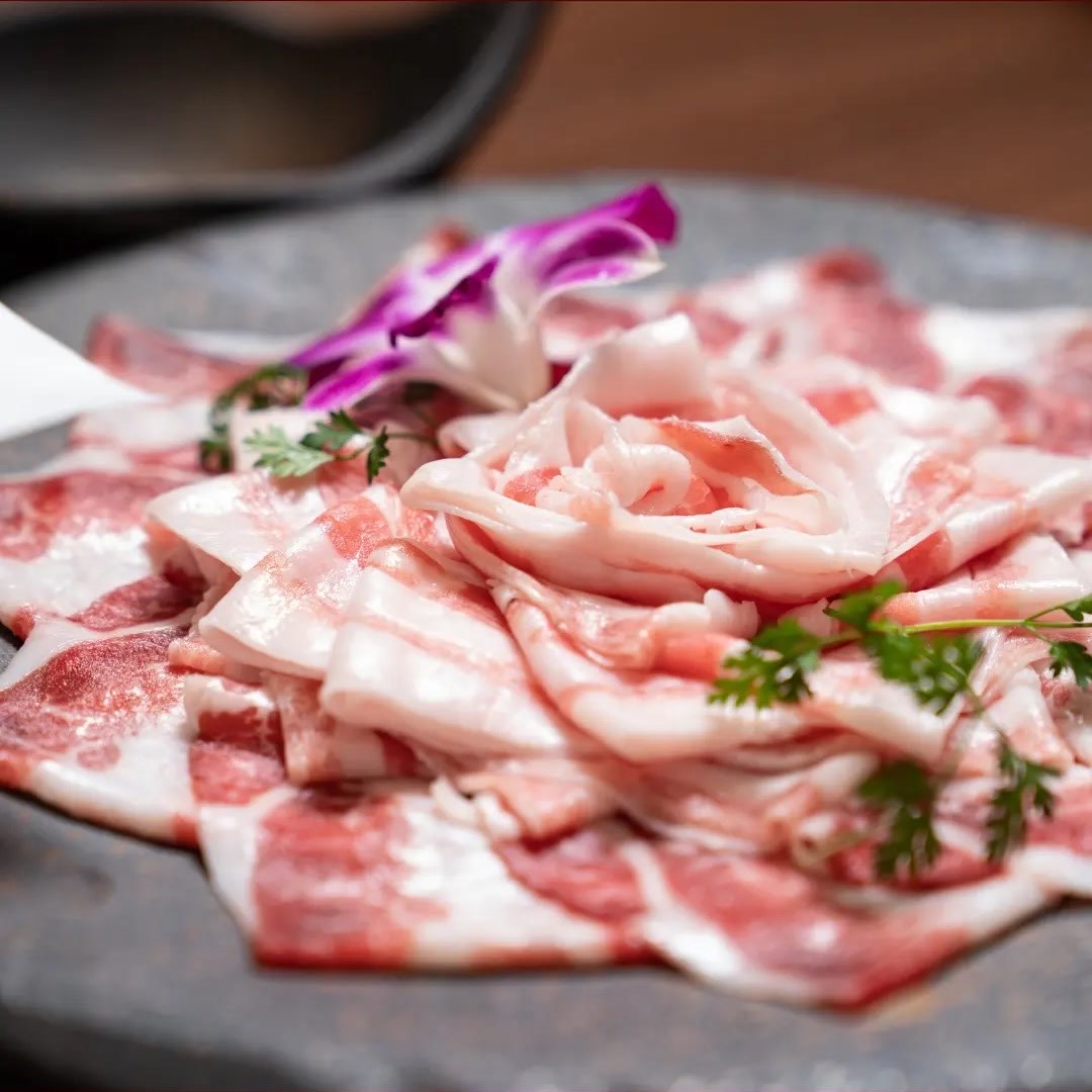 黒い皿に扇形に広げた霜降りの薄切り豚肉。セルフィーユと紫の蘭。
